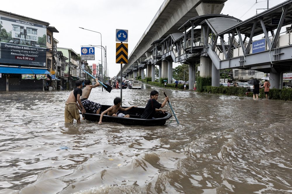 Überschwemmte Straße in Bangkok, junge Männer bewegen sich mithilfe eines Bootes fort