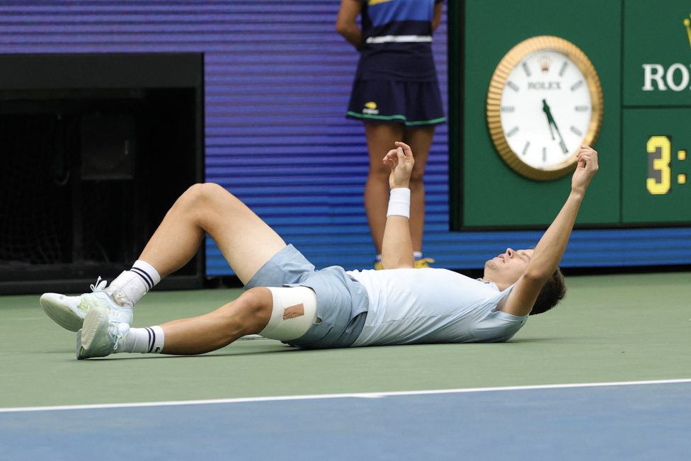 Alexander Blockx liegt erschöpft auf dem Rücken am Boden des Tennisfeldes, er streckt die Arme jubelnd in die Höhe