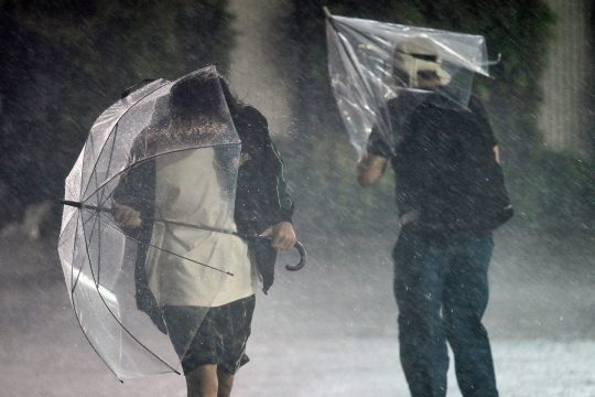 Menschen mit Regenschirmen kämpfen sich durch den heftigen Regen