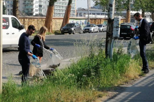 Menschen sammeln mit Mülltüten und Müllgreifern ausgestattet Müll an einem Grünstreifen