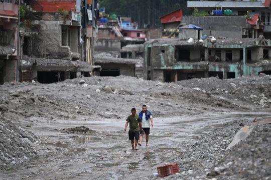 Überlebende in der nepalesischen Stadt Nuwakot laufen über eine von Schlamm überspülte Straße, vorbei an zerstörten Häusern