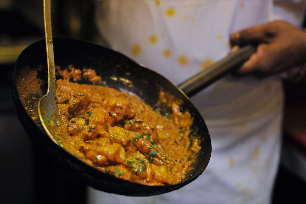 ein Mann schwenkt eine Pfanne mit einem Curry-Gericht