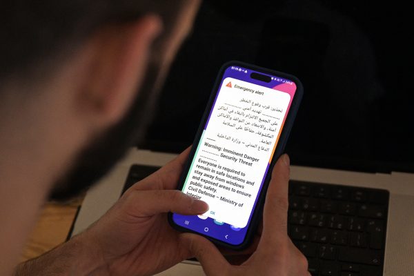 EinMann hält ein Smartphone in der hand, darauf ist eine Warnmeldung in arabischer und englische Sprache zu sehen
