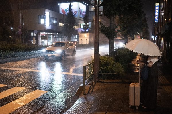 Frau miit Schirm wartet an Straße in heftigem Regen in Japan