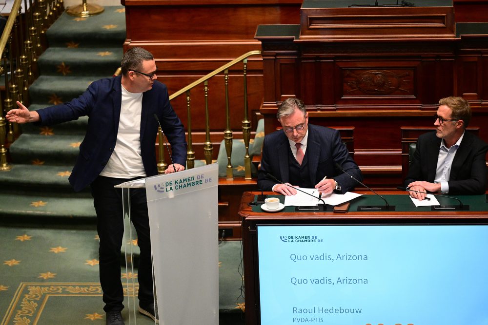 Premier De Wever und Paul Magnette sitzen am Tisch und folgen den Ausführungen von Raoul Hedebouw am Rednerpult