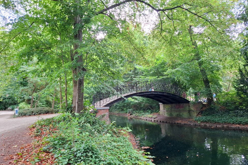 Eine Fußgängerbrücke führt über einen Wassergraben im Park