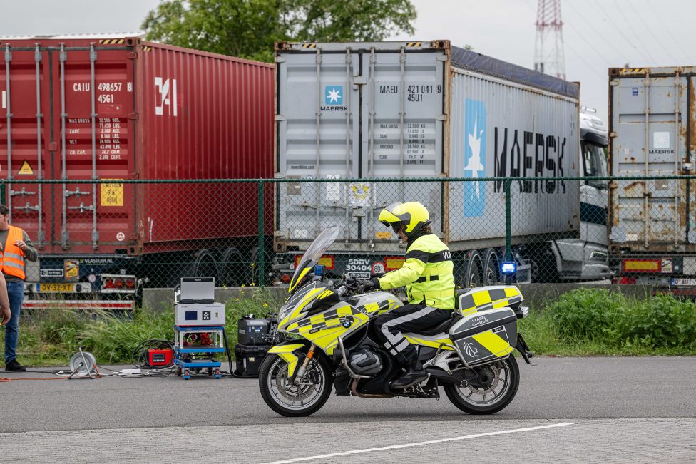 ein Polizist fährt auf einem Motorrad an mehreren LKW im Hafen vorbei