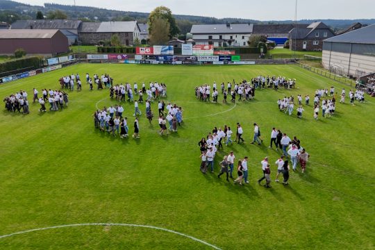 Blick von oben auf den Fußballplatz, auf dem dei Tänzer Kreise bilden