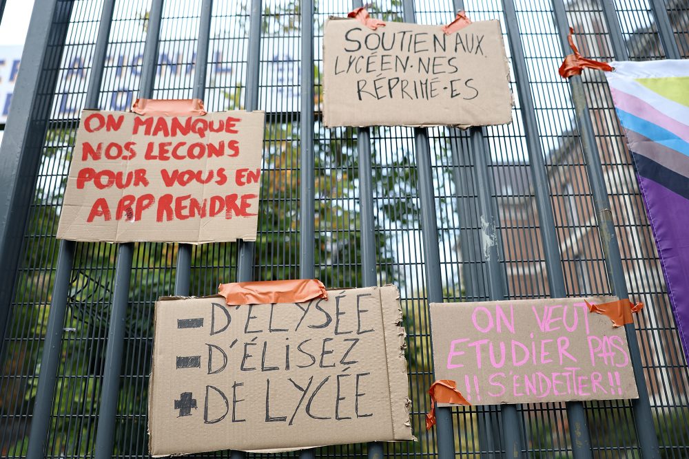Pappschilder hängen an einem Schultor - auf ihnen steht unter anderem geschrieben: „Wir versäumen unseren Unterricht, um euch zu unterrichten“, „Weniger Élysée, weniger Gewählte, mehr Gymnasien“ und „Wir wollen lernen, statt Schulden anzuhäufen“