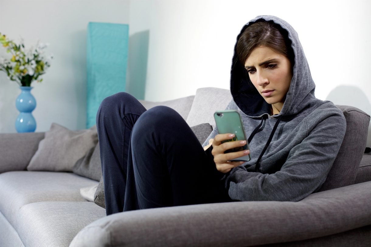 Junge Frau in Joggingkleidung sitzt mit Smartphone auf dem Sofa