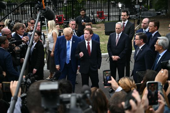 Meta-CEO Mark Zuckerberg spricht zu Pressevertretern, neben ihm steht US-Präsident Trump, im Hintergrund sind weitere Vertreter von Regierung und Tech-Branche