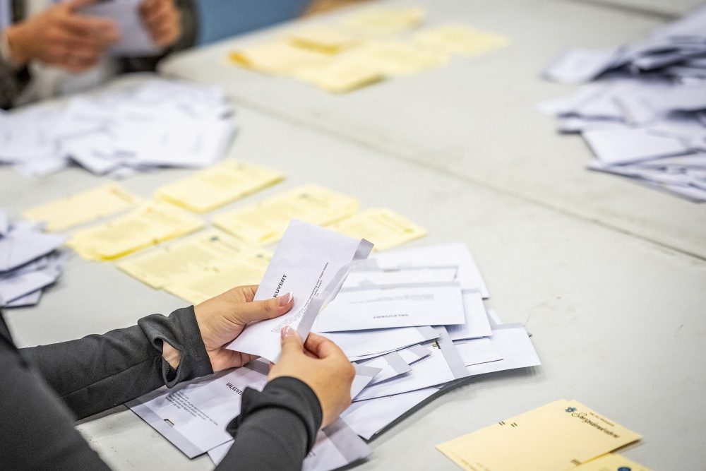 Hände öffnen Umschläge, auf dem Tisch weitere Umschläge und Wahlzettel
