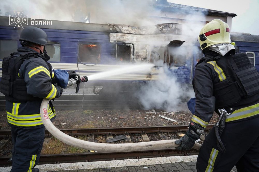 Feuerwehrleute besprühen einen beschädigten Zugwaggon mit Wasser