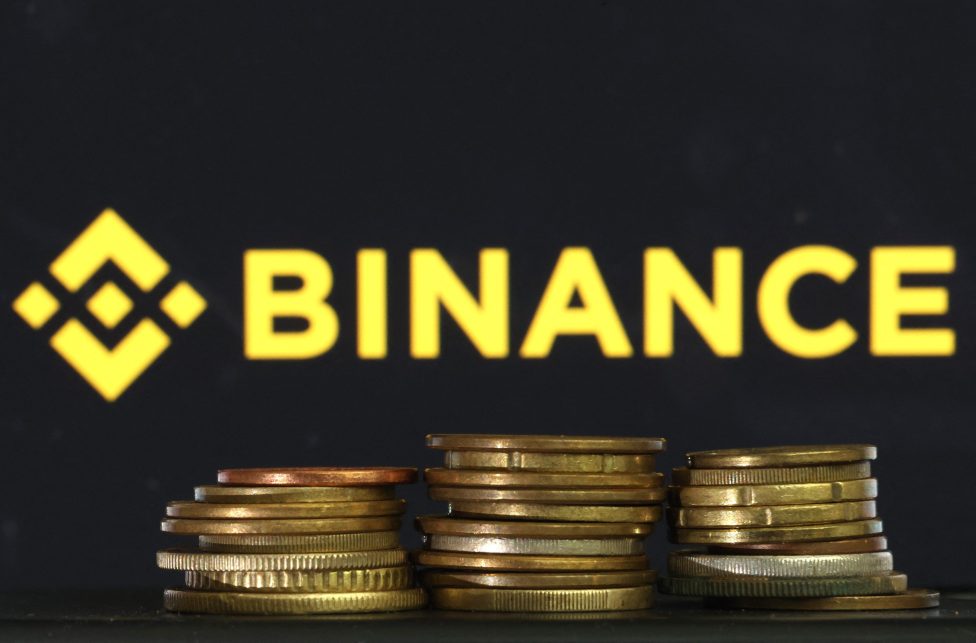 Logo und Schriftzug "Binance", davor liegen mehrere Euro-Cent-Müzen zu drei kleinen Türmen gestapelt