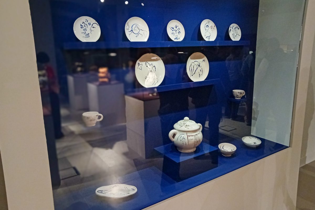 In einer Vitrine werden Teller, Schalen, eine Tasse und eine Kanne gezeigt