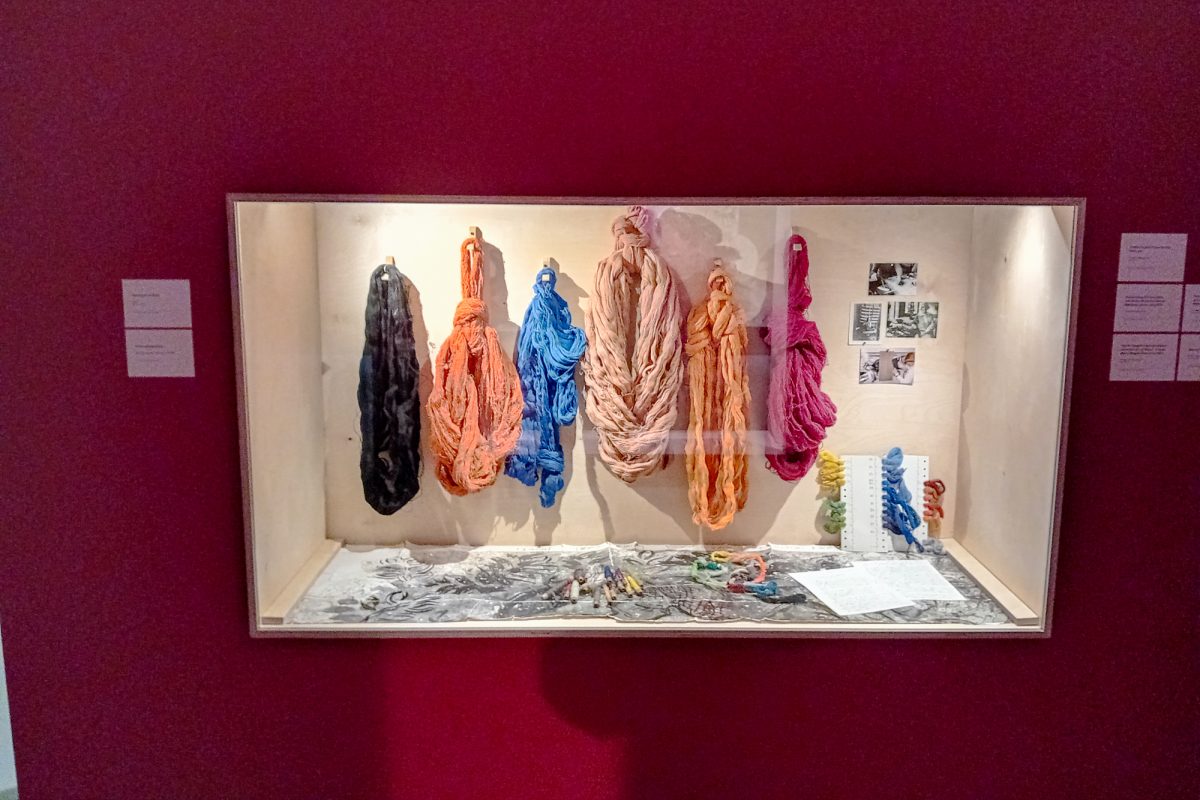 In einer Vitrine werden Ausstellungsstücke aus Stoffen in verschiedenen Farben gezeigt