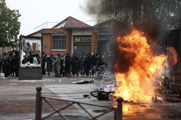 Mülltonnen und Fahrräder brennen, im Hintergrund Randalierer und Demonstranten vor einem Schulgebäude