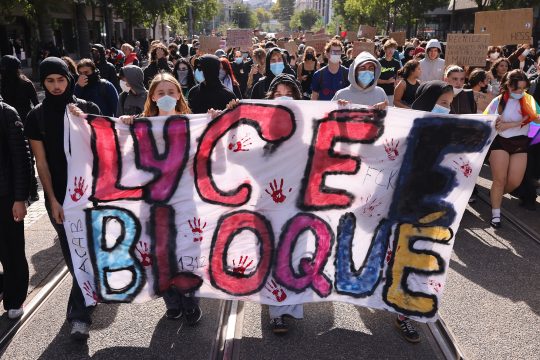 Schüler demonstrieren in Lyon, sie halten ein bemaltes Transparent in den Händen, auf dem in Französisch "Lycée Bloqué" steht