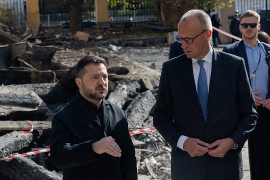 Der deutsche Bundeskanzler Friedrich Merz (re.) trifft bei seinem Besuch in Kiew den ukrainischen Präsidenten Selenskyj, im Hintergrund eine beschädigte Straße