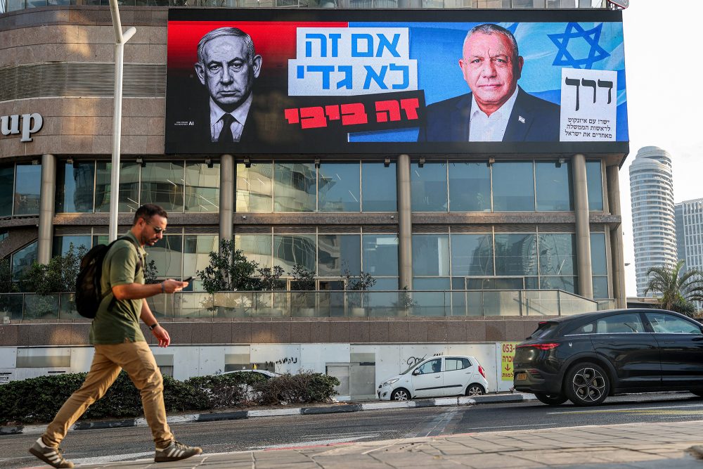 Ein Wahlplakat hängt an einem Gebäude, es zeigt die beiden Rivalen Netanjahu und Eisenkot - auf der Straße vor dem Gebäude geht ein Mann entlang