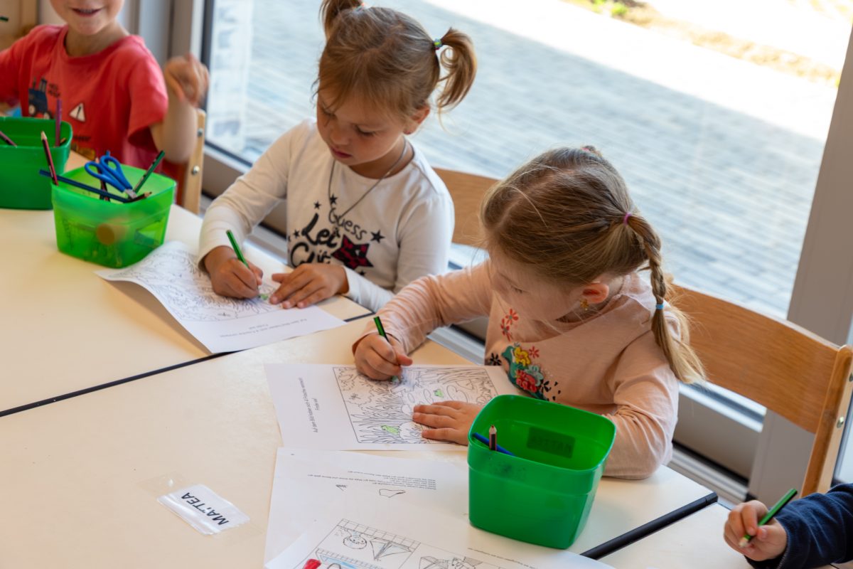 Kinder zeichnen mit Buntstiften auf einem Malbogen