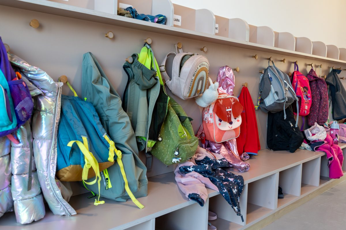 Rucksäcke und Jacken hängen an einer Garderobe
