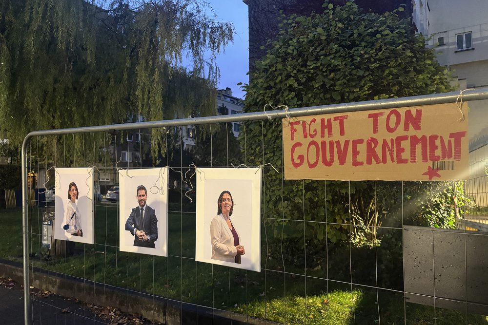 Ein Plakat mit der Aufschrift "Fight ton gouvernement" hängt an einem Bauzaun, daneben Fotos mehrere Minister