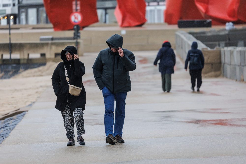 Zwei Spaziergänger halten ihre Kapuzen fest vor dem Sturm