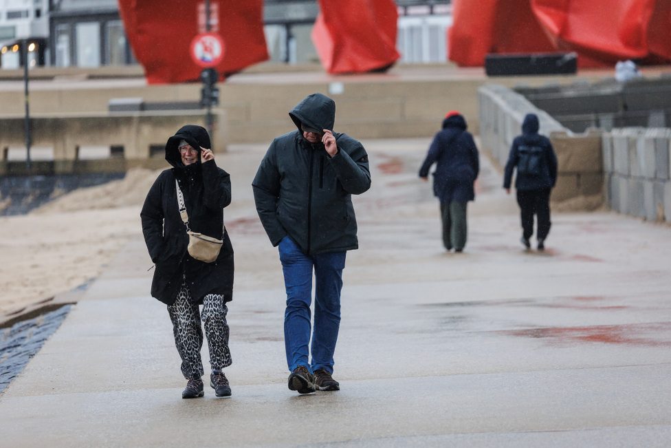 Zwei Spaziergänger halten ihre Kapuzen fest vor dem Sturm
