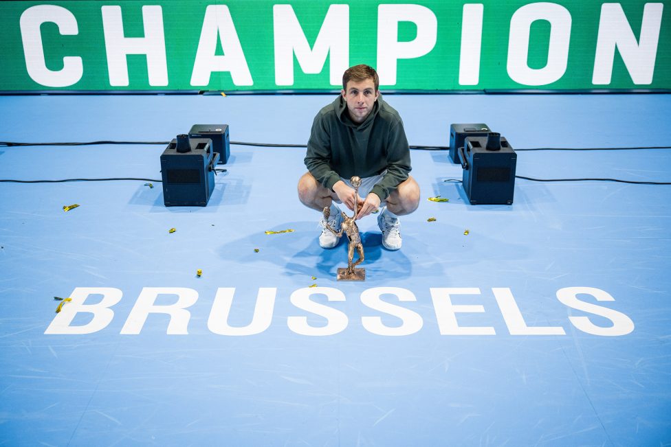 der Sieger hockt auf dem Boden, vor ihm auf dem Boden der Pokal und die Aufschrift "Brussels"