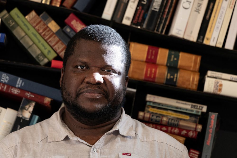 Thélyson Orélien vor einem Regal voller Bücher